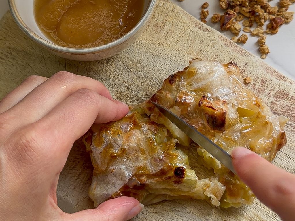 Baked apple pocket being sliced for breakfast, with apple filling and glaze.