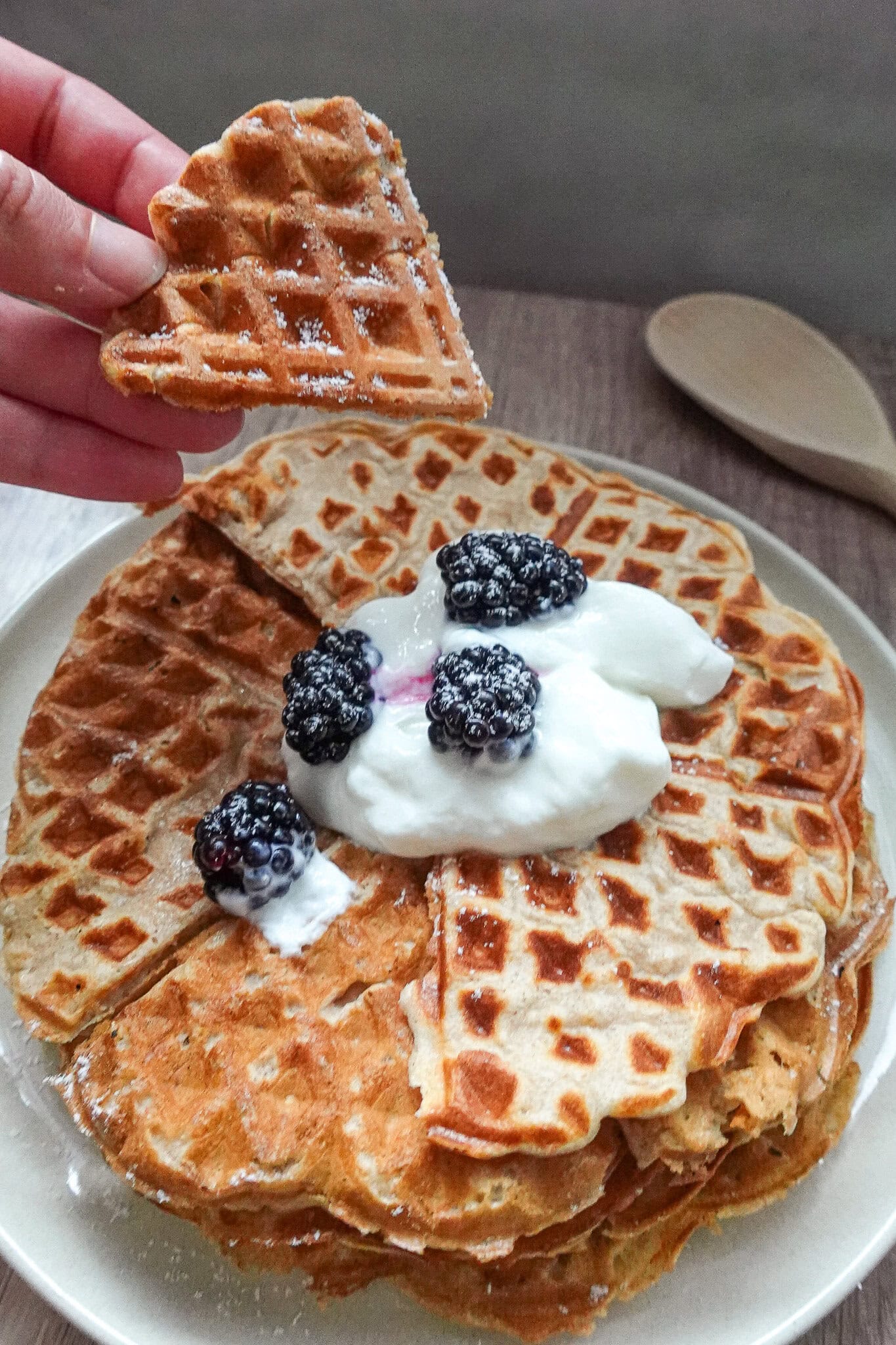 Stack of golden waffles topped with blackberries and whipped cream.