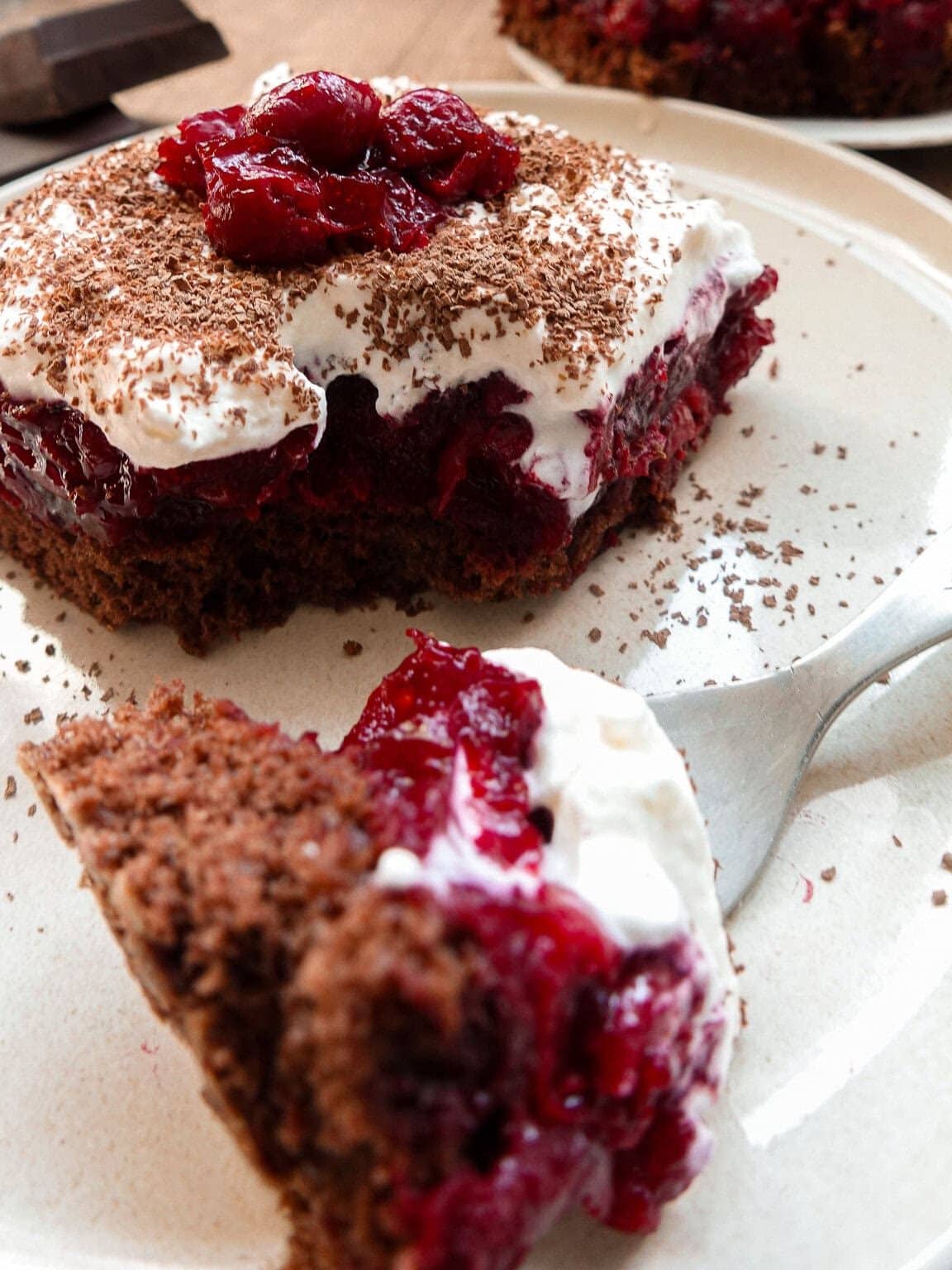 Cherry chocolate cake with whipped cream and cocoa powder.