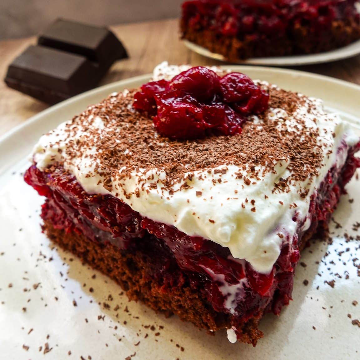 Close-up of a cherry chocolate cake slice with whipped cream and chocolate shavings.