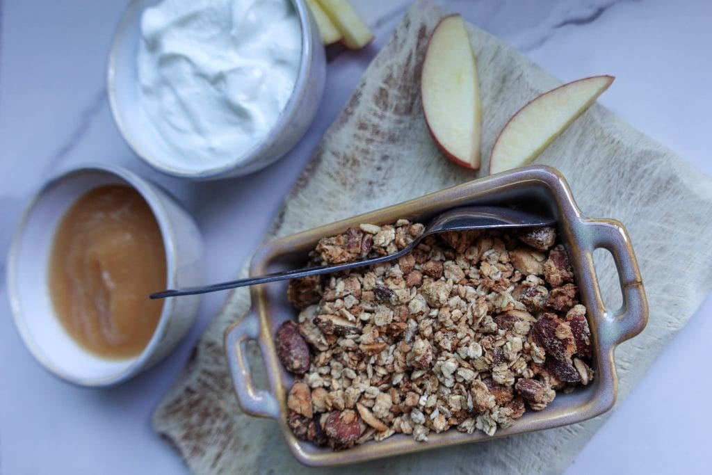 Crunchy homemade granola with apple slices and yogurt on a marble surface.