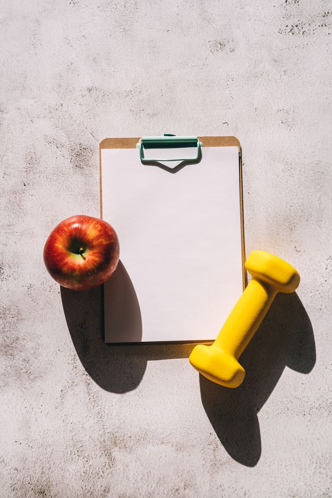 Apple and yellow dumbbell on a clipboard with blank paper for fitness planning.