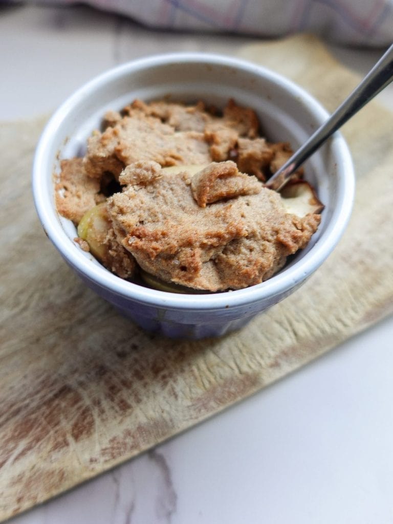 Homemade apple crumble in a small bowl with a spoon for two.