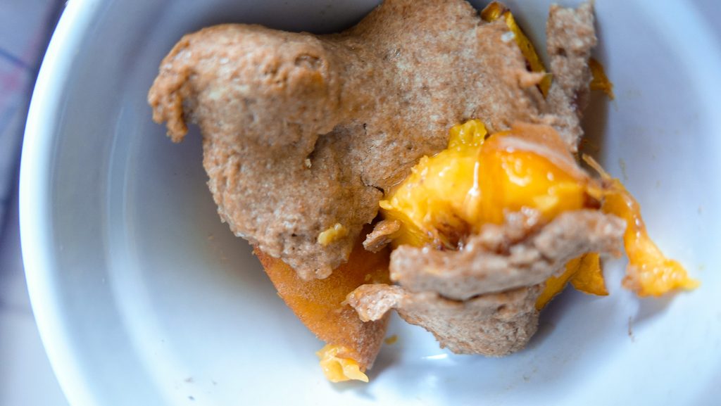 Close-up of peach crumble with melted peach filling in a white bowl.