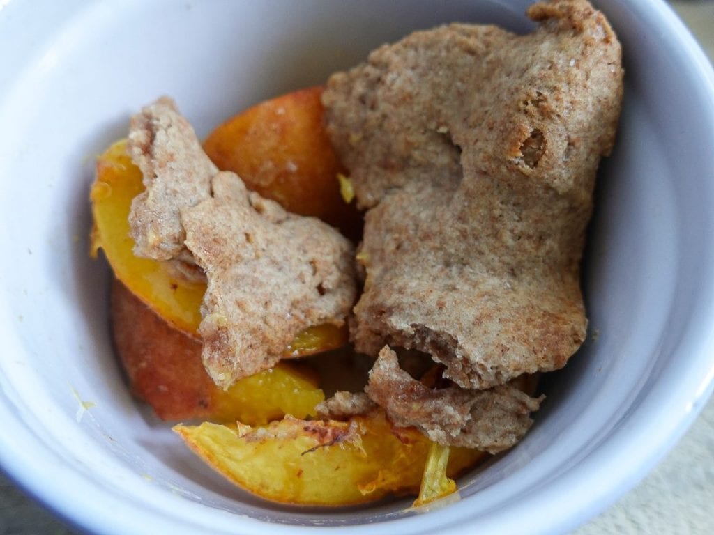 Small batch peach crumble with fresh peaches in a white bowl.