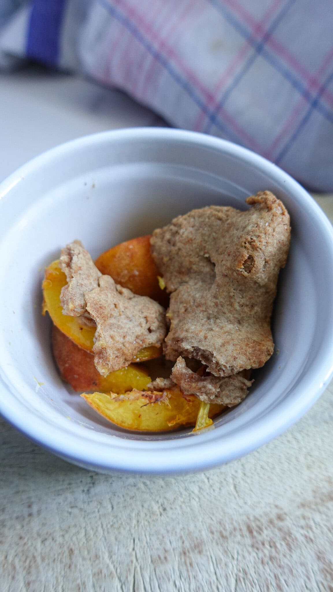 Small bowl of peach crumble with a biscuit topping, served warm.