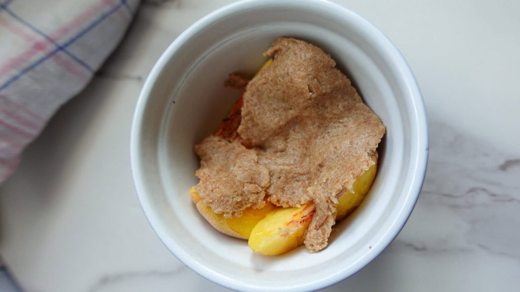 Mini peach crumble dessert in a white ramekin with crumble topping.