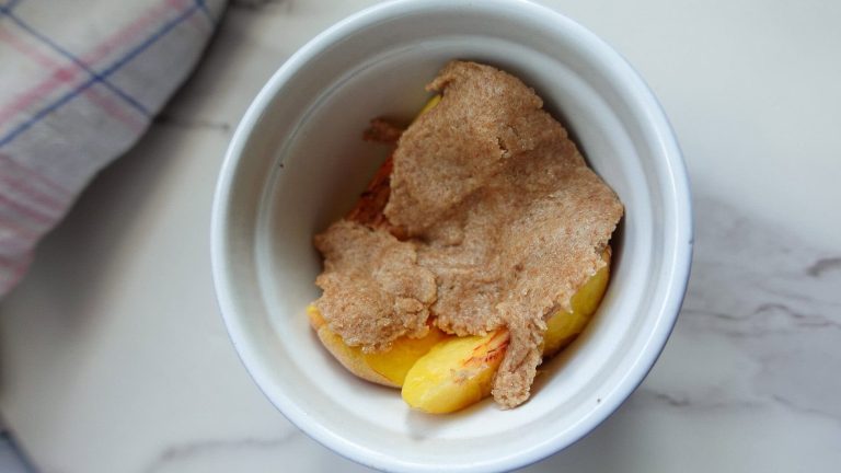Mini peach crumble dessert in a white ramekin with crumble topping.