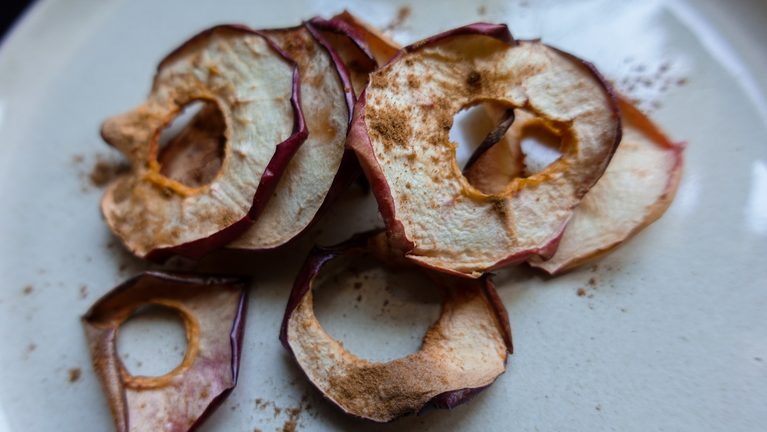Crispy homemade apple chips on a white plate, perfect for healthy snacking.