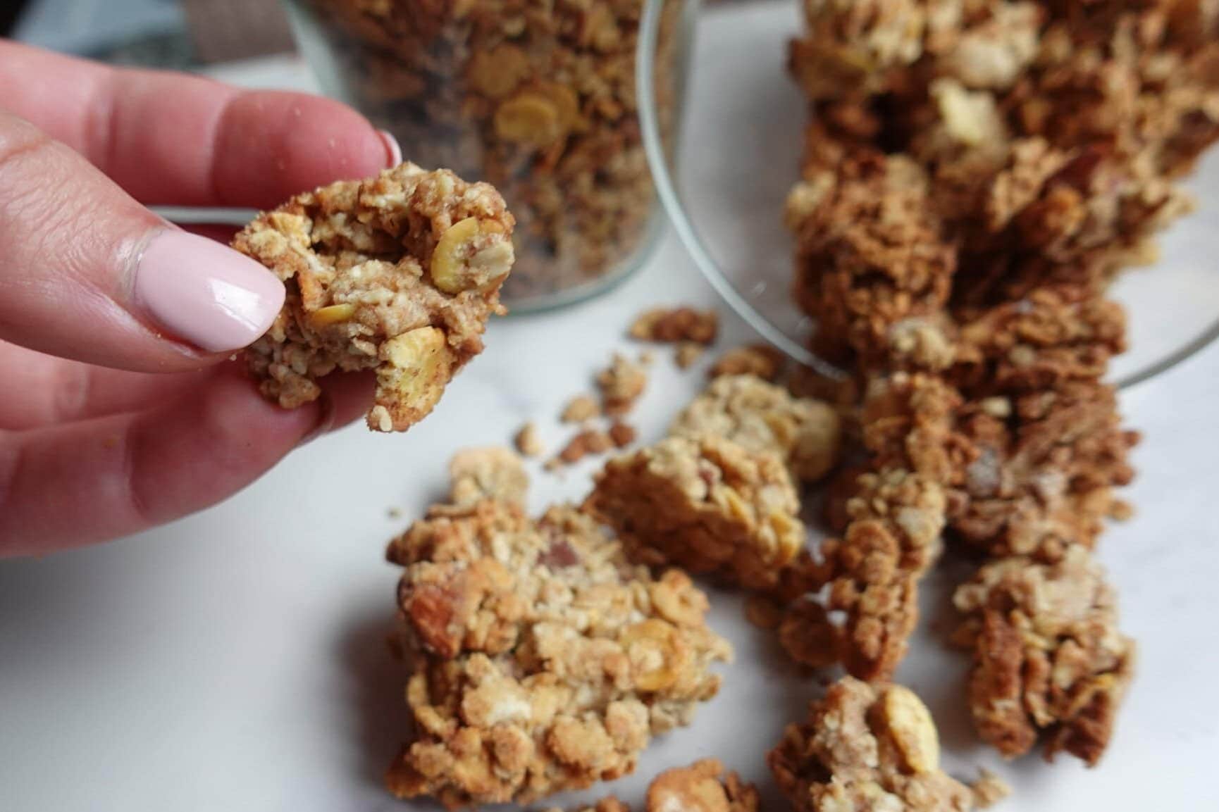Hand holding a piece of crunchy oat crumble with more on the table.