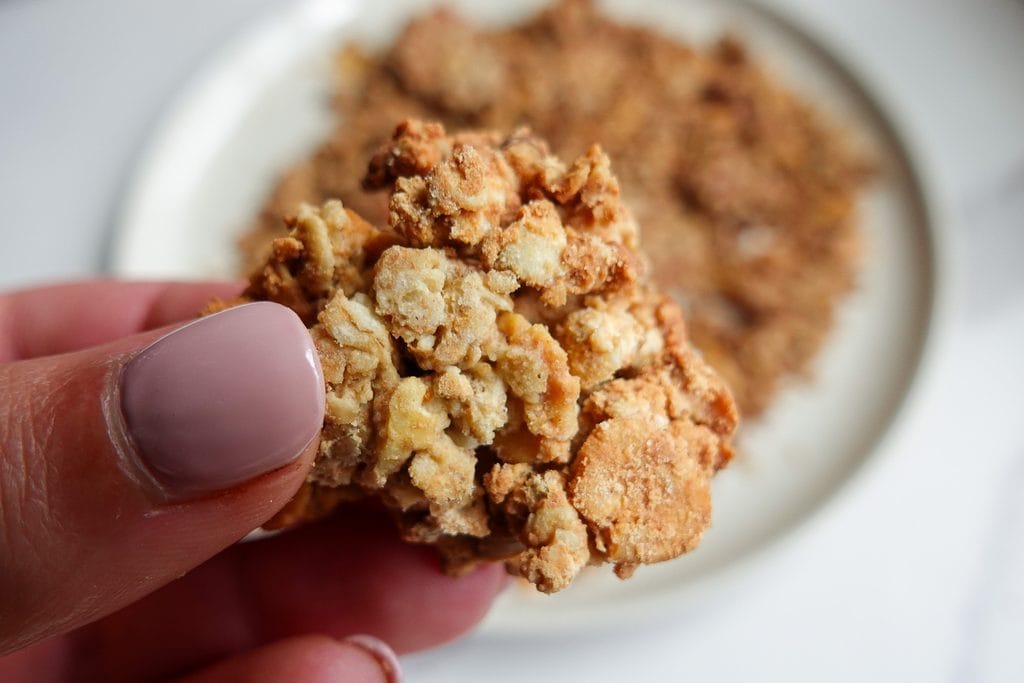 Close-up of a crunchy oat crumble bite held between fingers.