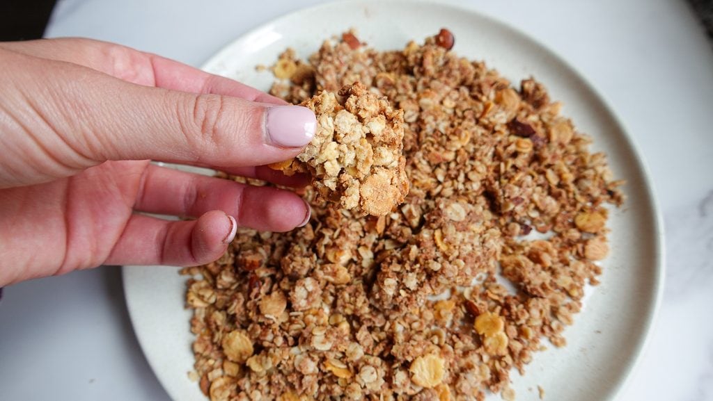Close-up of hand holding a crunchy granola cluster on a white plate.