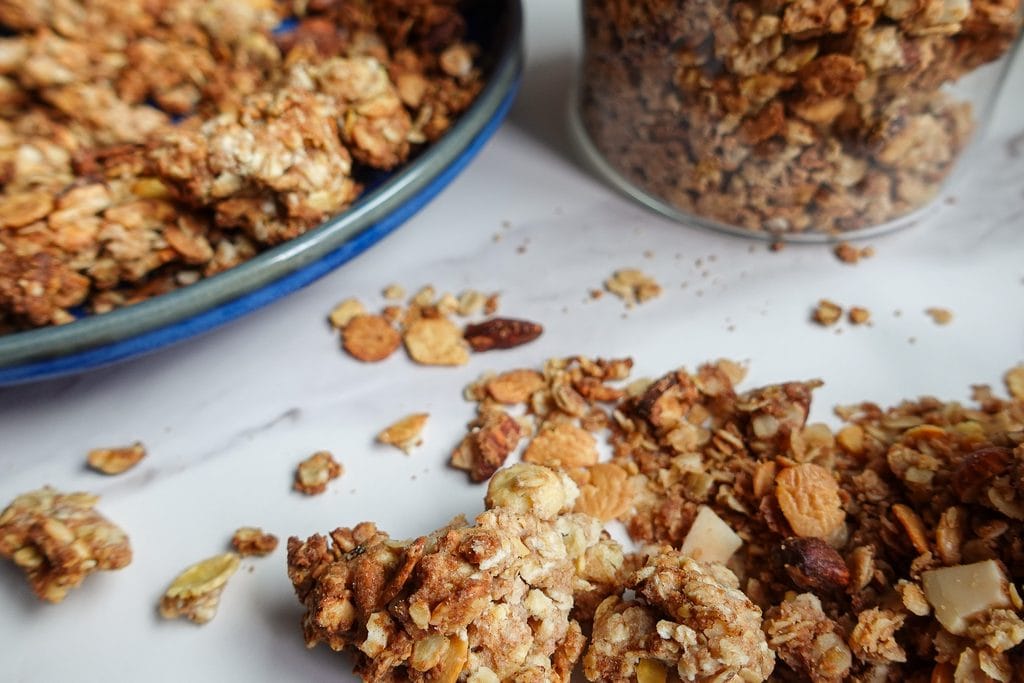 Crunchy homemade granola clusters with oats, nuts, and dried fruit on a white surface.