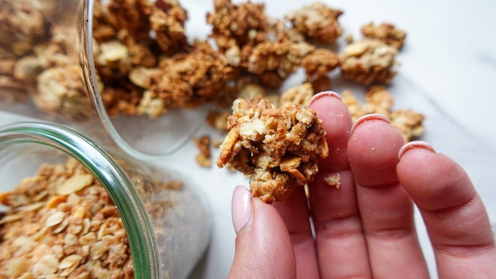 Close-up of a hand holding a crunchy granola cluster with more clusters in the background.